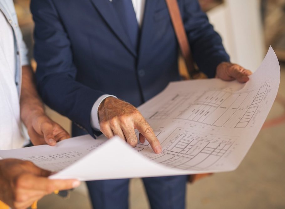 Two unrecognizable man holding architectural blueprint. One of them is pointing finger at the specific part.